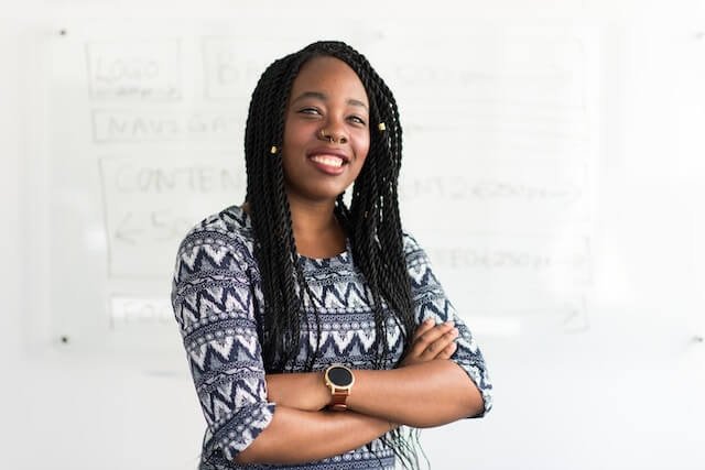 Photo of a smiling woman with long braided hair and arms crossed in front of her.